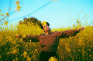 The musician Pachyman standing in a yellow field with his arms spread wide