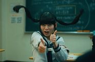 A girl with pigtails in school holds thumbs up.