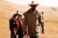 Man walks with horse on leash through a hilly plain.