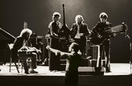 Black and white still from the film "The Last Waltz" (1978) showing a band performing with a conductor