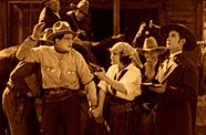 Western scene. Woman holds man in cowboy hat at gunpoint in sepia tone photo.