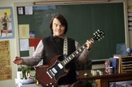 Jack Black stands wide eyed holding guitar. 