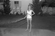 Black and white photo of a woman spraying the sidewalk with a hose