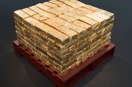 Pile of gold bricks sits atop a wooden pallet that has been painted dark red. 