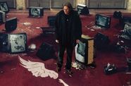 Man stands among broken tvs