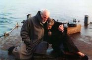 Man holds woman close while they sit by the ocean