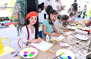 A girl with long brown hair wearing a red cap sits in front of a table with paint and miscellaneous craft items.