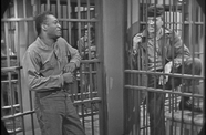 Two men speak to each other through prison bars