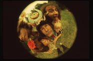A group of eccentrically dressed people look up from a glass plane into a fish-eye lens.