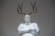 Life-size sculpture of a school principal standing with arms crossed, antlers growing from his head