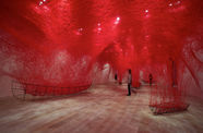 A huge intricate net of red thread creates a mesh over the gallery. Only coming down to connect with these iron wireframes of boats.