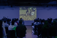 Audience sits in purple dim lit room watching a projected film