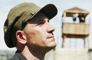 Still from Amerikatsi showing a man in closeup with a guard tower in soft focus behind him
