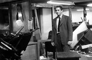 A man in a suit and tie stands in the middle of a trashed office
