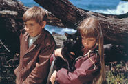 A boy and girl, both blond, the girl holding a black cat