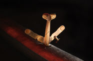 Film still of a brass airplane that's "crashed" into a piece of wood 