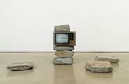 An old television set rests in the middle of a stack of large rocks, showing an image of two rocks on screen