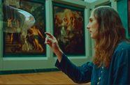 A man in a museum gallery reaching out to pop a big bubble.