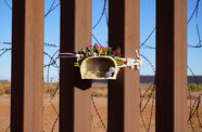 Ceramic figure holding flowers, tied to the US/Mexico border fence