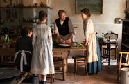 Four people in old garb stand around a dining table