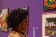 A smiling Black woman looks at art in a bright gallery