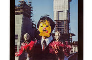 Photo of a man wearing a yellow mask reading "Psychic Self-Defense" carrying two miniature busts