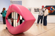 Gallery visitors look at a sculpture in the shape of a large mouth