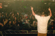 A DJ, seen from behind, plays for a large crowd