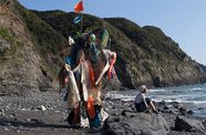 The artist Yangkura wearing a costume made of trash, standing on a beach