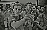 A White man, standing in front of a mob of people, points his finger angrily