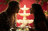 Two women, seen mostly in silhouette, speak in front of a three-tiered fountain