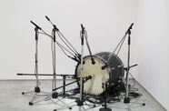 A bass drum sits on the floor surrounded by an array of microphones