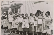A black-and-white photograph of ten women lined up with signs along the Citizenship Education Project's motorcade route encouraging voting and voter registration.