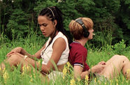 Two girls sit back-to-back in a field, wearing headphones