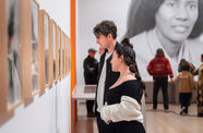 Visitors viewing a row of framed works installed on a gallery wall