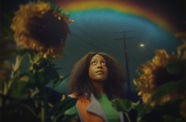 A Black woman, framed by sunflowers, looks up at a rainbow in the night sky
