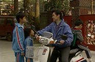 A woman on a motor scooter talks to two children in matching tracksuits