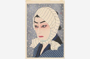 A Japanese woodblock print depicting the bust of a person in 3/4 view, looking to the viewer's left. The person has white skin, red lips, and dark shadows under the eyes, and wears a blue striped piece of fabric over the head and tied under the chin. The figure is wearing a blue striped shirt with black color, and the background is ligh tblue with small white circles as if to depict snow. At upper right is Japanese caligraphy and a red real. 