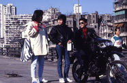 Three youths, one sitting on a motorcycle, in a city