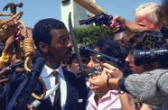 A Black man in a suit is surrounded by press