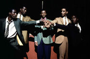 Five Black men stand in a semi-circle, their hands joined in the center
