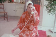 A woman in a pink robe kneels on the phone as she talks into a telephone