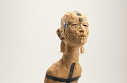 Ceramic figure with long earrings, body enveloped in beaded necklaces