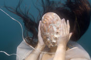 A woman, underwater, holds a large shell in front of her face