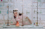 Olivia Rodrigo looks intently at a glass beaker while wearing a vintage nurse outfit