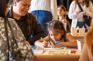 Child draws at a table while adults look on
