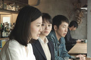 Two women and a man, viewed in profile, sit at a bar counter