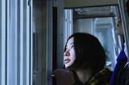 A woman with a short, dark bob haircut looks out of a window