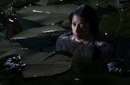 A dark-haired woman stands neck-deep in a body of water, surrounded by large plant fronds