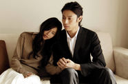 A mand and woman sit on a couch holding hands
